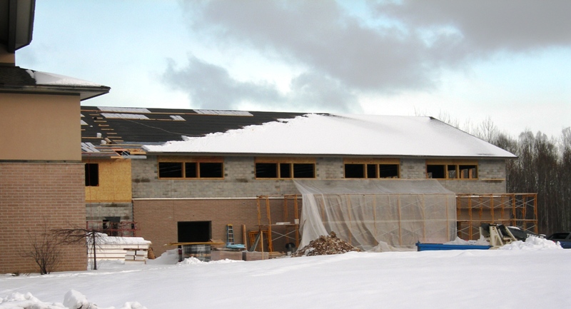 picture of rear elevation shows roof installation progress on addition - snow covers part of the roof and window framing is under way