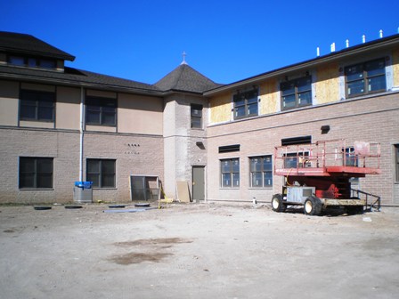 picture of two-story Church Addition with mason's lift parked next to wall being worked on - the masonry has been installed up to the second level, below the window ledge at the clerestory