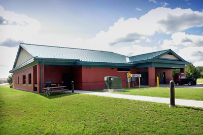 picture of covered rear entry and covered outdoor break area at Billeting Services Building, Alpena Combat Readiness Training Center - the building has red brick walls with cream colored masonry accents, blue/green metal roof and tinted windows