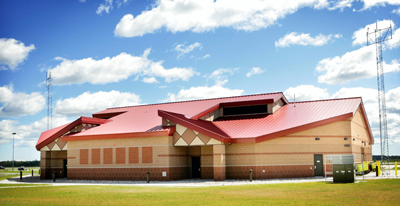 picture of front entry elevation of Squadron Operations Facility at Alpena Combat Readiness Training Center - this uniquely shaped building is concrete masonry unit walls with red metal roof