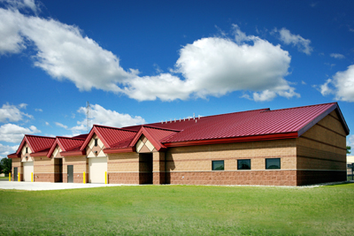 picture of Squadron Operations Facility at Alpena Combat Readiness Training Center - runway elevation of building constructed of concrete masonry unit walls in shades of tan and brown, with a red metal roof