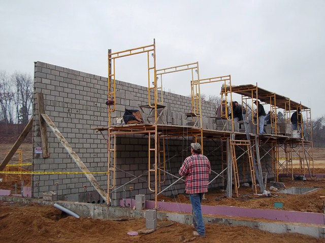 Workmen on scaffold building concrete masonry unit wall