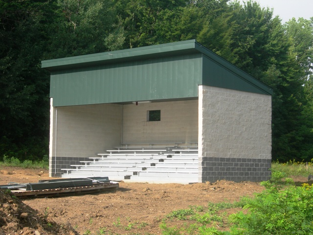 picture of open front bleacher enclosure with decorative cmu walls, green metal roof and trim