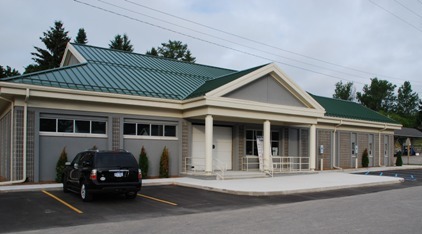 picture of exterior of Littlefield-Alanson Area Community Library - Main Entrance - building is grey masonry with white trim and green metal roof