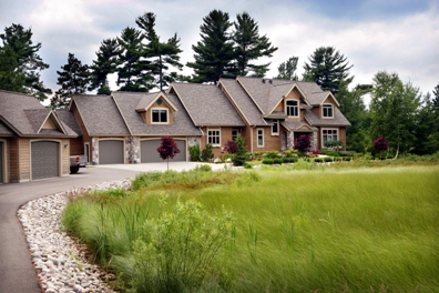 picture of lakeside custom home on Otsego Lake - this exterior photo was taken from the road-side of the home, coming up the driveway toward the front of the home - the naturalized prarie grass along the driveway provides a sharp contrast to the traditional landscaping at the front of the home
