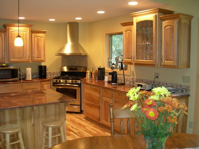 interior photo of custom kitchen - light wood tone custom cabinets, drop lights and pendant lighting, granite counters, stainless range hood