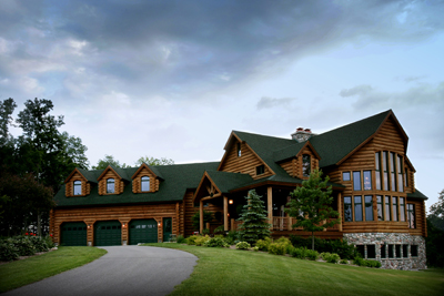 exterior photo of custom log home in Gaylord Michigan - front elevation from driveway approach - natural log siding, green architectural shingled roof, fieldstone lower level