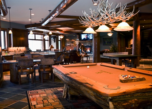 this interior photo is of the lower level game room with a hanging antler light fixture above the rough hewn custom pool table