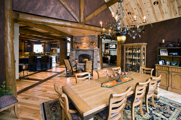 interior photo of dining room with views into kitchen beyond - high wood beam and plank ceiling, wood beam walls and wood floors
