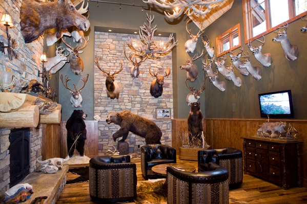 photo of 'Trophy Room' high walls displaying mounted hunting trophies surrounding seated area in front of fireplace