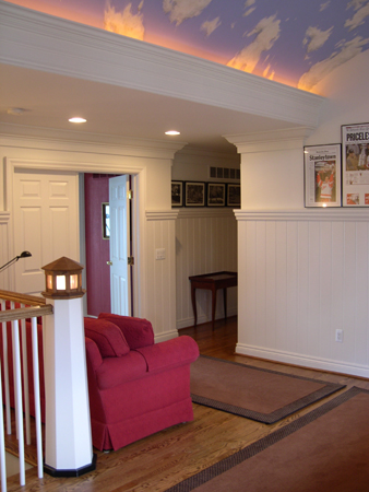 this interior photo is of the home's upper level landing - the curved ceiling has perimeter lighting recessed in the crown molding and partly cloudy sky-motif paint, stair railing has nautical theme elements with a lighthouse inspired newel post