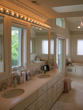 this interior photo is of the master bath for the home, showcasing the custom room-length vanity with double sink and tons of counter space - a window in the center of the vanity wall between the mirrors which are over the sinks brings in natural light to the space, as does the overhead skylight, french door to deck and window over the spa tub