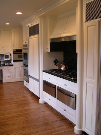 this interior photo is of the home's gourmet kitchen, showing the custom cabinets and built in appliances - the cabinet fronts are duplicated for the refrigerator/freezer doors, range hood and stove front/double oven drawer fronts - formal columns flank the stove construction and recessed lighting softly illuminates the space