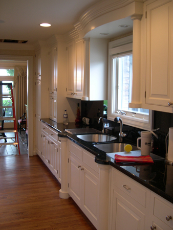 this interior photo is of the home's gourmet kitchen counter area showing custom cabinets, crown molding and formal columns flanking a double sink - the black countertop provides contrast to the white cabinets and ceiling while the wood floor provides warmth