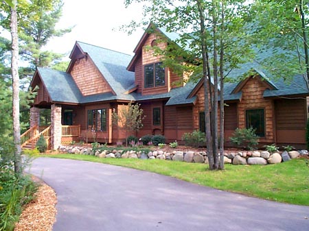 picture of golf course home - this exterior photo is of the home's front elevation showing cedar shake siding, green architectural shingle roof and covered porch with stone clad pillars