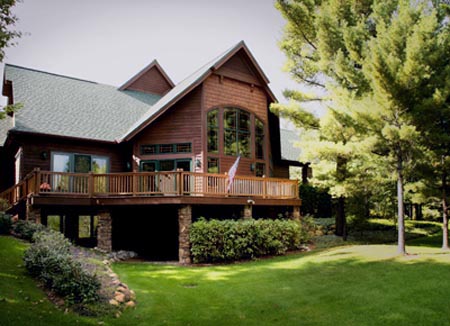 picture of golf course home - this exterior photo is of the home's side elevation showing outdoor decking that extends around the rear of the home, supported by stone clad pillars