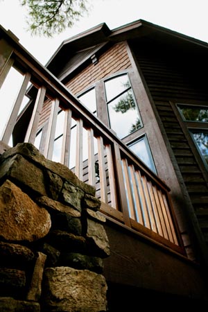 picture of golf course home - this exterior photo was taken while standing at ground level, from beside the outdoor deck's supporting fieldstone pillar, looking up at the deck rail and upper level window wall