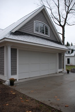 picture of lakeside home in Topinabee, Michigan - this exterior photo facing the garage is taken from the road-side elevation, showing dark grey siding and roof with white trim and custom window for bonus room above garage