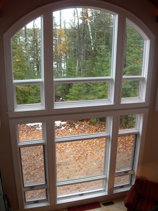picture of waterfront home on Twin Lakes in Cheboygan, Michigan - this interior photo was taken from the second floor, looking out toward the custom double-high window with curved upper panels in the living room - from this angle you can see the lake through the trees