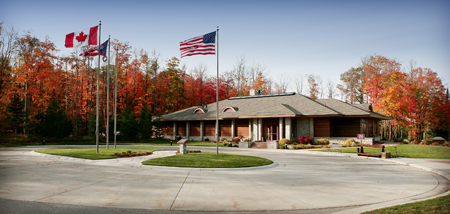 exterior picture of UAW Black Lake Golf Course Clubhouse - main entrance and circular drive, with flags flying in foreground and Autumn trees in background