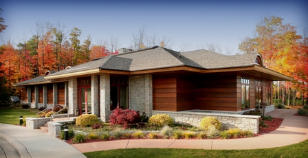 exterior picture of UAW Black Lake Golf Course Clubhouse main entry and side patio - dark wood siding, stone accents and wood trim, grey roof with backdrop of autumn leafed trees